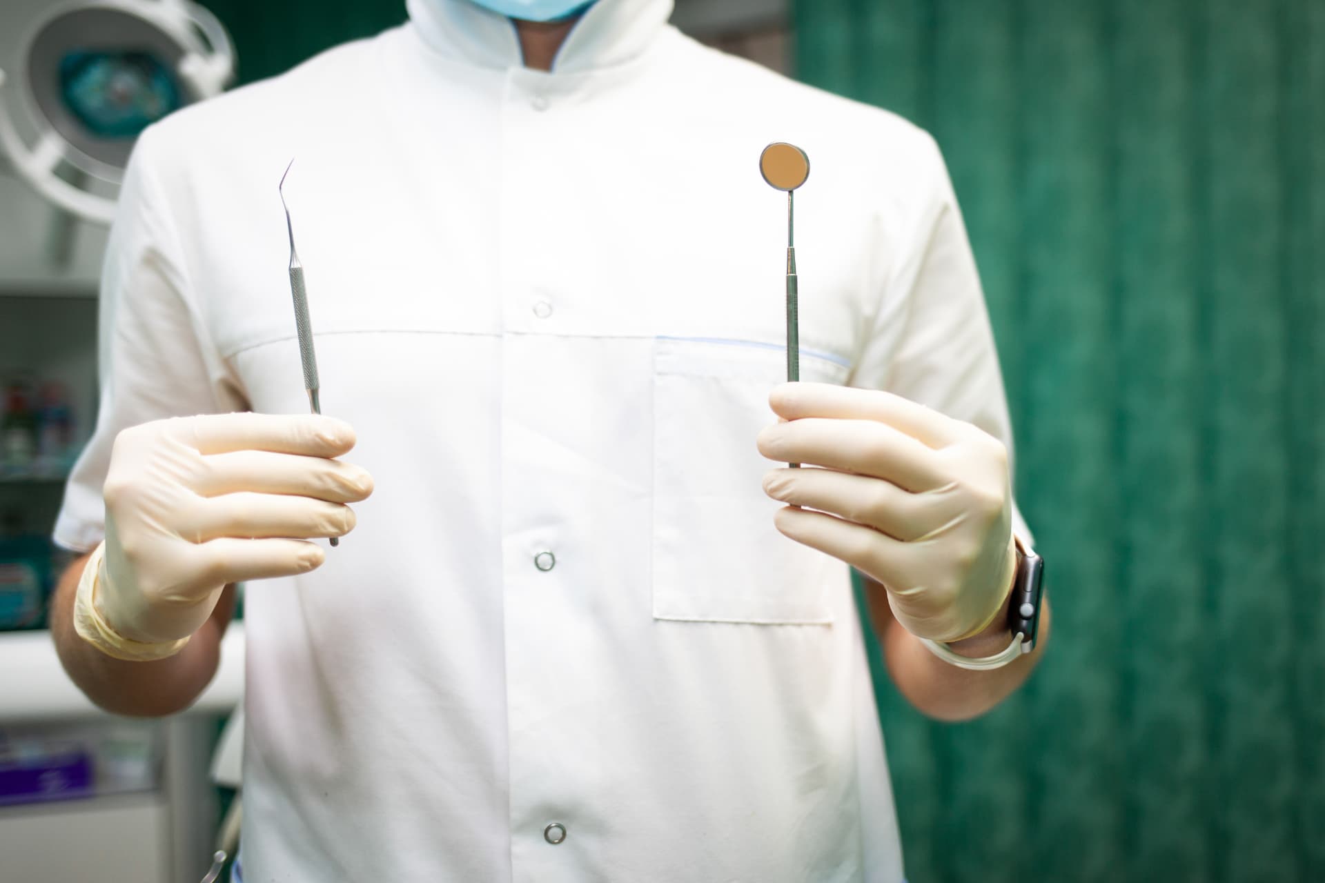Dentist holding a dental explorer and examination mirror in a treatment room
